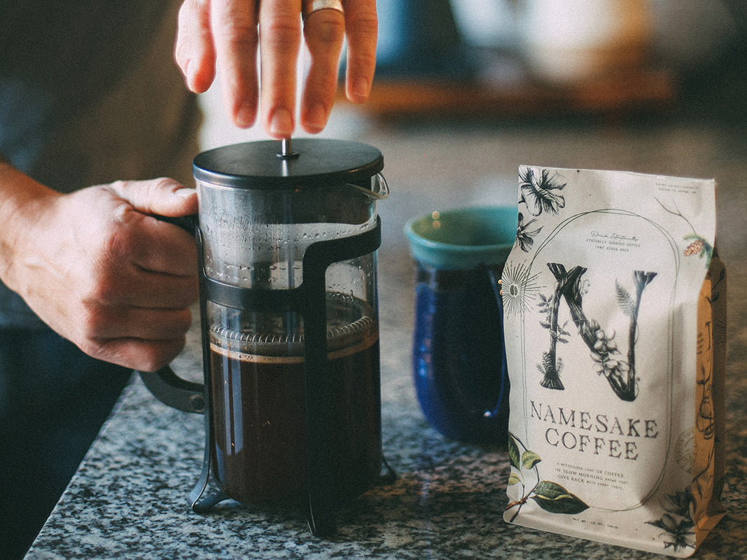 Man pressing down the French Press, with the Namesake coffee bean bag next to it on the counter.